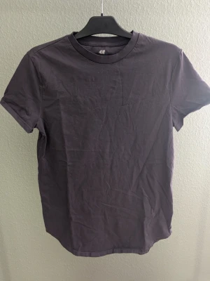 Grå basic t-shirt från H&M - En grå t-shirt från H&M i modellen Long Fit. Klassisk rund halsringning och korta ärmar. Tillverkad i mjuk bomull som känns skön mot huden. Perfekt till jeans eller shorts för en clean och enkel look.