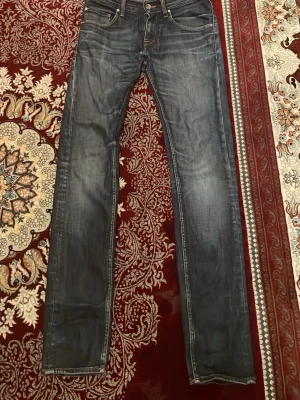 Mörkblå skinny jeans med slitningar - Snygga mörkblå jeans från Tiger of sweden med slim passform W27 L32 och diskreta slitningar på framsidan och baksidan. Klassisk femficksdesign och smal siluett som sitter tajt längs benen. Jeansen är tillverkade i jeansmaterial och har en modern look som passar till sneakers eller boots.