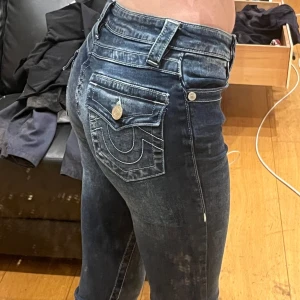 Mörkblå utsvängda jeans med broderad bakficka - Snygga mörkblå jeans med låg midja och broderad bakficka. De är Bootcut och har klassisk femficksdesign med knappar och dragkedja framtill. Perfekta för en stilren look. Midja 35, Innerben 82