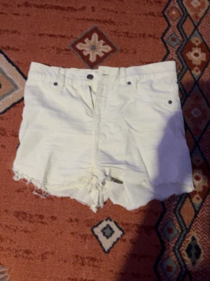 Vita shorts från Fabulous - Vita shorts från Fabulous i modell med medelhög midja och råa, fransiga kanter. Klassisk femficksdesign och knappgylf. Perfekta för sommaren och riktigt snygga till crop tops eller oversized t-shirts. Säljes då de är för stora för mig och kommer ej till användning.