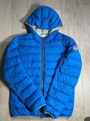 Blå Colmar pufferjacka med huva - Säljer en blå pufferjacka från Colmar med huva och dragkedja framtill. Jackan har ett quiltat mönster och Colmar-logga på ärmen. Perfekt för kyliga dagar och riktigt skön att bära. Passar dig som gillar sportig och enkel stil.