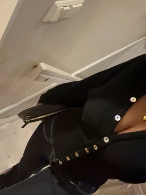 Svart kofta från Gina Tricot - Säljer en svart, croppad kofta från Gina Tricot med v-ringning och silvriga knappar framtill. Koftan har bred ribbad midja och långa, lite vidare ärmar. Stickad i mjukt material som passar perfekt till jeans eller kjol.