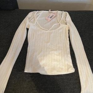 Vit ribbad långärmad topp från Nelly  - Säljer en vit långärmad topp från Nelly i storlek XS. Toppen har smala axelband och en snygg offshoulder-design med ribbad struktur. Materialet är mjukt och stretchigt med en figurnära passform. Oanvänd med lappen kvar. 
