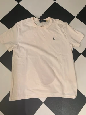 Ralph Lauren T-shirt - Klassisk begie t-shirt från Polo Ralph Lauren. T-shirten har rund hals, korta ärmar och den ikoniska broderade loggan på bröstet. Skulle inte säga att det är XL utan mer som M-L