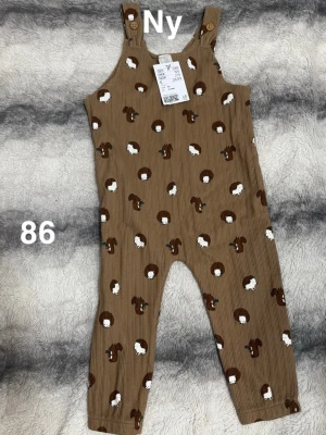 Bruna byxdress med igelkottar och ekorrar - Supersöt brun byxdress med tryck av igelkottar och ekorrar. Byxdressen har ribbad struktur, knappar på axelbanden. Perfekt för dig som gillar gulliga djurmotiv och bekväma plagg.🌸 Så mjuka och sköna. Nya. Storlek 86