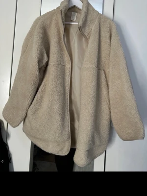 Beige teddyjacka från Carin Wester  - Mysig beige teddyjacka från C.W. med hög krage och dragkedja framtill. Jackan har en oversized passform och är gjord i fluffigt teddy-material som håller dig varm under kyliga dagar. Perfekt att slänga på sig över en hoodie eller t-shirt.