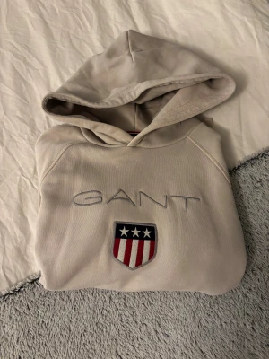 Ljusrosa hoodie från GANT - Snygg ljusrosa hoodie från GANT med broderat logotyp och ett coolt emblem med stjärnor och rödvita ränder på bröstet. Tröjan har huva, magficka och ribbade muddar💗