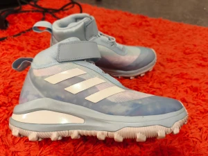 Adidas Frozen II sneakers ljusblå - Säljer ett par Adidas Frozen II sneakers i ljusblått med vita detaljer och klassiska tre ränder på sidan. Skorna har grov sula med hjärtformade dobbar, kardborreband och dragflik bak. Perfekta för dig som gillar Disney och vill sticka ut med snygga detaljer.
