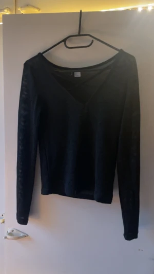 Svart v-ringad tröja från Divided - Svart långärmad tröja från Divided i storlek S. Tröjan har en snygg v-ringad hals och är tillverkad i ett lätt stickat material som känns skönt mot huden. Perfekt för dig som gillar enkel och stilren design.