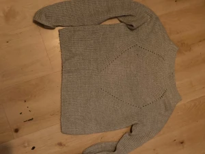 Beige stickad tröja från Hollis - Säljer en beige stickad tröja från Hollis i storlek S. Tröjan har ett snyggt hålmönster i form av en diamant på framsidan och är ribbstickad över hela. Den har långärmade ärmar och en klassisk rund hals. Perfekt för dig som gillar enkel och stilren design.