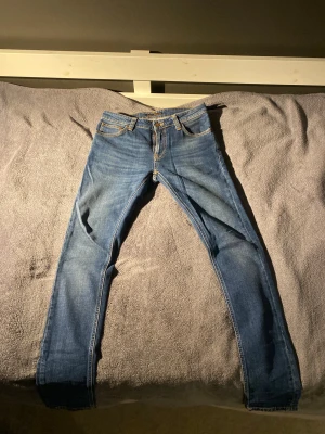 Blå jeans från Nudie Jeans - Snygga blå jeans från Nudie Jeans med klassisk femficksdesign och kontrastsömmar. Storleken är W27 L32. Tveka inte på att fråga om du undrar något
