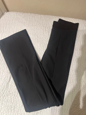 Svarta högmidjade kostymbyxor från Zara - Snygga svarta kostymbyxor från Zara med satin detaljer vid midjan och veck. Byxorna är högmidjade och lite längre i längden. I storlek S!