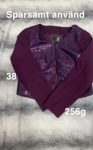 Lila paljettbolero från bonprix  - Snygg lila cardigan bolero från bonprix med glittriga paljetter framtill och enfärgade långärmade partier. Boleron har rund halsringning och är perfekt för dig som vill sticka ut med lite extra bling. Passar dig som gillar att vara trendig och unik.🌸 Sparsamt använd. Storlek 38