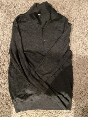 Mörkgrå stickad polotröja Uniqlo S - Snygg mörkgrå stickad polotröja från Uniqlo i storlek S. Tröjan har en hög krage, knappar framtill och långa ärmar. Perfekt för dig som gillar stilrena och enkla plagg med en chill vibe. Materialet är mjukt och känns skönt mot huden. Fräsch, utan defekter. 