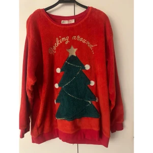Röd jultröja med julgran från H&M - Röd långärmad jultröja från H&M med mjukt (mjukare) Teddy-fleecematerial. Framsidan har en stor grön julgran med guldstjärna och paljettdetaljer, samt texten 'Rocking around...' broderad i guld. Perfekt för att maxa julkänslan! Alla paljetter finns kvar, även att de inte syns på bild. Oversize i storleken.