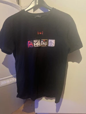 Svart Dsquared2 t-shirt med tryck - Svart t-shirt från Dsquared2 i bomull med coolt tryck framtill som visar olika motiv och logga. Klassisk rund hals och korta ärmar. Perfekt för dig som gillar streetwear och vill sticka ut lite extra.