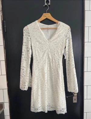 Vit spetsklänning från Bubbleroom S - Superfin vit spetsklänning från Bubbleroom med v-ringning och långa utsvängda ärmar i spetstyg. Köpte förra året till studenten men blev en annan klänning. Så den är helt ny med prislapp aldrig använd. 