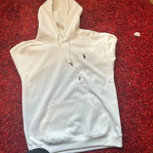 Vit hoodie från Polo Ralph Lauren - Snygg vit hoodie från Polo Ralph Lauren med klassisk broderad logga på bröstet. Tröjan har huva med snörning, känguruficka och långa ärmar. Tillverkad i mjuk bomull som känns skön mot huden. Perfekt för en clean och stilren look. Det står på den att den är Xl men passar bra i M och L 