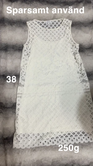 Vit spetsklänning i storlek 38 - Superfin vit klänning i storlek 38, med vackra spetsdetaljer och blommigt mönster. Ärmlös och med rund halsringning, perfekt för dig som gillar romantisk stil. Klänningen är lätt och har en snygg kort längd.🌸Sparsamt använd. Storlek 38