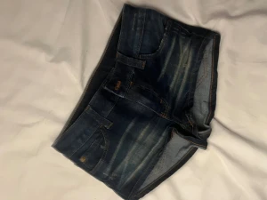 Mörkblå jeansshorts med slitningar - Snygga mörkblå jeansshorts med slitna detaljer och klassiska fickor fram och bak. Shortsen har en lågmidjad passform och är perfekta för varma sommardagar. De har synliga sömmar och en cool tvättad look.