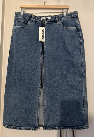 Blå jeanskjol med dragkedja från Kappahl /Nytt skick! - Snygg blå lång jeanskjol från Kappahl i klassisk denim med rak passform. Kjolen har framfickor, bälteshällor och en cool dragkedja framtill som går hela vägen ner och slutar i en slits. Perfekt för dig som gillar enkel och stilren denim.
