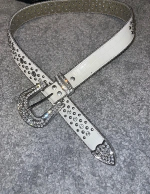 Rhinestone belt - Säljer ett rhinestone bälte med glittrande strass på både spänne och spets. Skärpet har ett croco-mönstrat yttre och är dekorerat med silvriga nitar och stenar längs hela remmen. Perfekt för dig som vill sticka ut och addera lite  till din outfit. Bältets totala längd är 147cm vilket motsvarar S