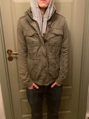 Mörkgrön field jacka från Abercrombie & Fitch  - Riktigt snygg field jacka från Abercrombie & Fitch med fyra fickor framtill, hög krage och dragkedja med knappstängning. Jackan är i storlek S. Vid frågor och funderingar, fråga på! 