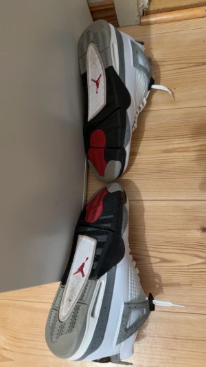 Nike Air Jordan 4 White Cement sneakers - Nike Air Jordan 4 White Cement sneakers med vit ovandel i skinn, grå och svarta detaljer samt röda inslag på tungan och sulan. Klassisk meshpanel på sidorna, snörning och ikonisk Jumpman-logga. Grå stänkmönster på häl och sula, samt Nike Air branding bak. Storlek 44 säljer de eftersom de ej passar pris kan diskuteras.
