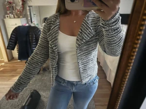 Svartvit stickad cardigan jacka - Säljer en svartvit stickad cardigan jacka med dragkedja framtill. Jackan har ett snyggt mönster och är långärmad med en lite croppad passform. Perfekt för dig som gillar en chill och trendig look. Passar till jeans och t-shirt för en enkel stil.