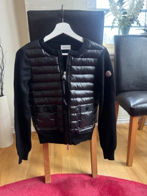 Svart Moncler cardigan  - Helt oanvänd Snygg svart cardigan från Moncler med snygg framsida och två fickor med knappstängning. Jackan har långärmade stickade ärmar och ribbad krage. Dragkedja framtill och Moncler-logga på ärmen. Passar Xs men även S. Skriv vid frågor/funderingar.