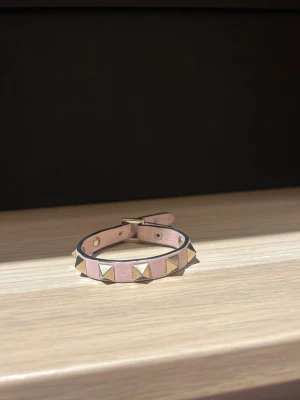 Rosa armband med guldnitar - Snyggt rosa armband med pyramidformade guldnitar runt hela bandet. Armbandet har en stilren design med justerbart spänne och svarta kanter som ger en cool kontrast. Perfekt accessoar för att lyfta din outfit med lite edge. Den saknar en liten bit för att hålla fast bandet men det är enkelt att fixa! Köptes för ungefär 3000kr så säljer mycket billigare.