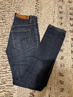 Tiger of Sweden Ruby jeans blå 27/32 - Snygga mörkblå jeans från Tiger of Sweden, modell Ruby Gracious. Klassisk femficksdesign med bruna detaljer och logopatch i läder baktill. Raka ben och normal passform, tillverkade i slitstarkt bomullsjeansmaterial.