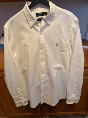 Polo Ralph Lauren skjorta slim fit - Vit skjorta från Polo Ralph Lauren i slim fit med klassisk krage och knappar framtill. Broderad logga på bröstet och långa ärmar med manschett. Skjortan är gjord i mjuk bomull och har en clean, stilren look som funkar till många olika outfits. 