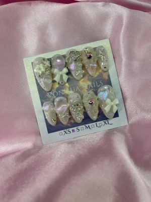 BabyShoujo (S);Medium Almond - Säljer ett set med handgjorda press-on naglar i ljusrosa och pärlemor med holografiska detaljer. Naglarna har 3D dekorationer som rosetter, blommor, hjärtan och strass i silver och rosa. Formen är almond och materialet är akryl. Perfekt för dig som vill ha extra glam.
