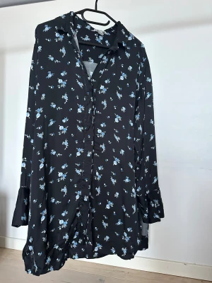 Skjorta från H&M - Svart långärmad skjorta med blått blommönster och knappar framtill. Skjortan har en lös passform, krage och är tillverkad i viskos.    Obs: Alla plagg säljs endast fram till 28/12 