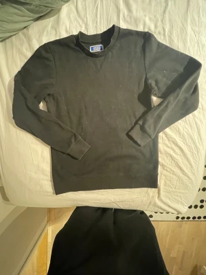 Svart sweatshirt från Jack & Jones - En stilren svart sweatshirt från Jack & Jones med rund hals och långa ärmar. Tröjan har en klassisk passform och är gjord i mjuk bomull, perfekt för chill dagar. Ribbstickade muddar vid ärmslut och nederkant ger en snygg finish.
