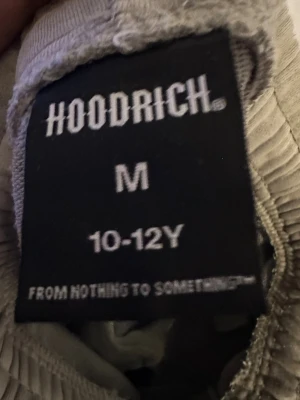 Grå Hoodrich shorts med ficka och tryck - Snygga grå shorts från Hoodrich med elastisk midja och snörning. De har en praktisk ficka på sidan med coolt tryck i svart och gult. Perfekta för chill dagar och streetwear-stil. Materialet är mjukt och känns skönt mot huden.
