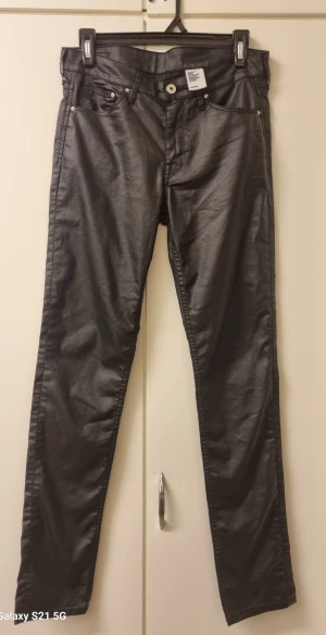 Svarta skinny byxor med glans - Snygga svarta byxor från H&M med skinny passform och glansig finish som ger en cool look. Klassisk femficksmodell med dragkedja och knapp framtill. Materialet är syntet och bomull, vilket gör dem både bekväma och stilrena.