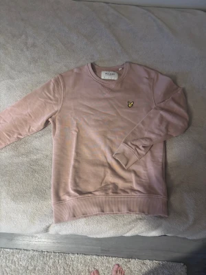  sweatshirt från Lyle & Scott - Säljer en  sweatshirt från Lyle & Scott med klassisk rund hals och ribbade muddar. Tröjan har det ikoniska gula fågelmärket broderat på bröstet och är tillverkad i ekologisk bomull. Perfekt för chill dagar och enkel att matcha med jeans eller joggers.