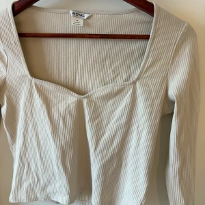 Beige ribbad topp från Monki - Säljer en beige ribbad topp från Monki med lång ärm och snygg fyrkantig ringning. Toppen är croppad och har en lätt figurnära passform. Perfekt att styla med jeans eller kjol för en trendig look.