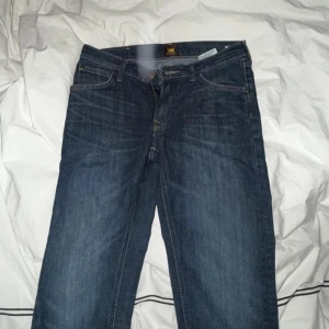 Mörkblå jeans från Lee W29 L32 - Snygga mörkblå jeans från Lee med klassisk femficksdesign och tydliga sömmar. Jeansen har rak passform och är tillverkade i slitstarkt denimtyg. Perfekt för dig som gillar en enkel och tidlös look.