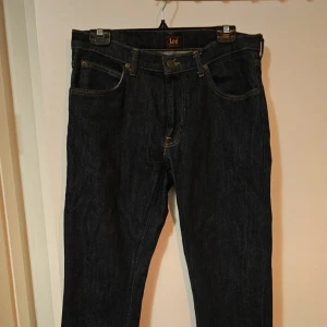Mörkblå jeans från Lee W32 L30 - Snygga mörkblå jeans från Lee med klassisk femficksdesign och kontrastsömmar. Modellen har rak passform och normal midja, tillverkade i slitstarkt denimtyg. Perfekta för dig som gillar stilrena och tidlösa jeans. W32 L30