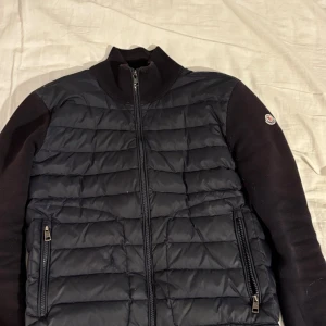 Moncler cardigan  - Svart moncler cardigan lite solbränd, pytte litet hål som man inte tänker på i helheten, nfc scan funkar