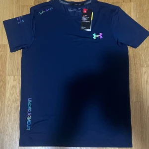 Blå Under Armour HeatGear t-shirt - Snygg marinblå t-shirt från Under Armour med färgglatt logotryck på bröstet. som passar M/L