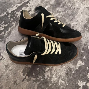 Maison Margiela Gats  - Säljer ett par Maison Margiela German Army Trainers i den klassiska svarta färgen. Storlek 43 och passar true to size. Det här är min favoritfärg – stilrena och tidlösa sneakers.  Skorna är endast lätt använda och i väldigt bra skick. Köpta direkt från Maison Margiela och kvittot osv finns kvar. Originalbox och dustbags medföljer (kortet som kom med har tyvärr kommit bort).  Ett riktigt fint par som är lite för stora för mig. Pris: 3450 kr – eller bud.