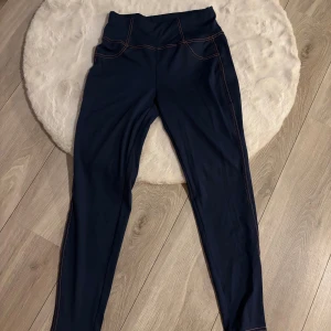 Mörkblå leggings från SHEIN, S - Snygga mörkblå leggings från SHEIN med orange kontrastsömmar och två bakfickor. Hög midja och stretchigt syntetmaterial som sitter tight och bekvämt. Perfekta för sportiga outfits eller chill dagar. 