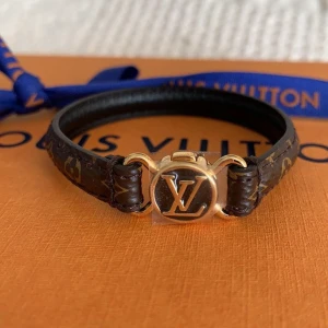 Louis Vuitton monogram armband Clic It Bracelet - Snyggt armband från Louis Vuitton med klassiskt monogrammönster i brunt och guld. Armbandet har en rund LV-logga i svart och guld framtill och är gjort i läder med exklusiva detaljer. Perfekt accessoar för dig som gillar lyxig och tidlös stil. Pris kan diskuteras vid snabb affär, kvitto o box finns självklart!