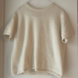 Beige stickad tröja Gina Tricot - En enkel och stilren beige stickad tröja från Gina Tricot. Modellen har korta ärmar, rund hals och en mjuk, lite loose passform. Perfekt för dig som gillar en clean look och vill ha något bekvämt och snyggt till vardags. Enstaka noppror 