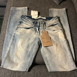 Superlågmidjade jeans - Säljer ett par ljusblå raka jeans från Jeanswear 72D, modell Regular. Jeansen har snyggt slitna detaljer, och dragkedja med knapp. Materialet är jeans och passformen är rak med låg midja. Storleken är W26 och passar perfekt på mig som är 165 lång.