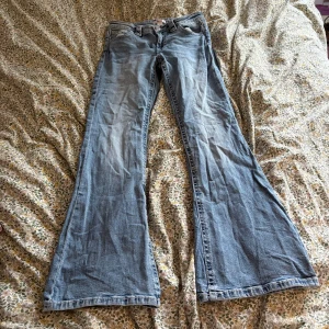 Blå low waist bootcut jeans från Gina Tricot Young - Snygga ljusblå jeans från Gina Tricot Young i bootcut-modell med klassisk femficksdesign och knappstängning. Jeansen har en lätt tvättad look och är tillverkade i mjukt denimtyg som ger en skön passform. Perfekt för dig som gillar retrovibbar och breda ben.